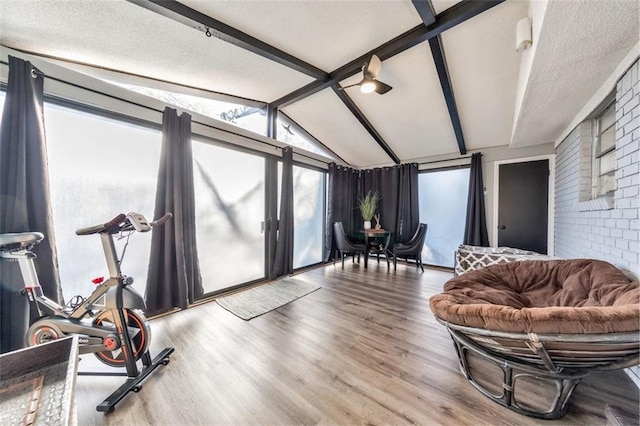 interior space with brick wall, a textured ceiling, hardwood / wood-style floors, and vaulted ceiling with beams