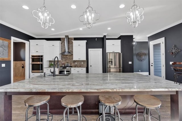 kitchen featuring white cabinetry, appliances with stainless steel finishes, wall chimney range hood, and a large island with sink