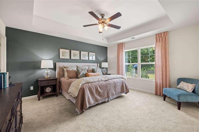 bedroom featuring ceiling fan, a tray ceiling, and light carpet