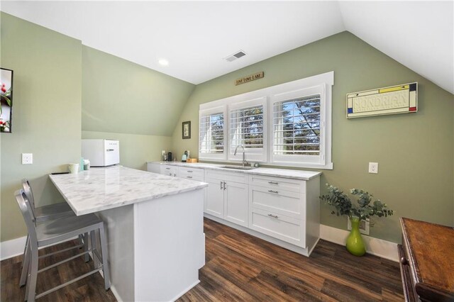 4115 Merritt Dr, Cumming, GA 30041 - kitchen featuring vaulted ceiling, a breakfast bar, white cabinetry, sink, and dark wood-type flooring