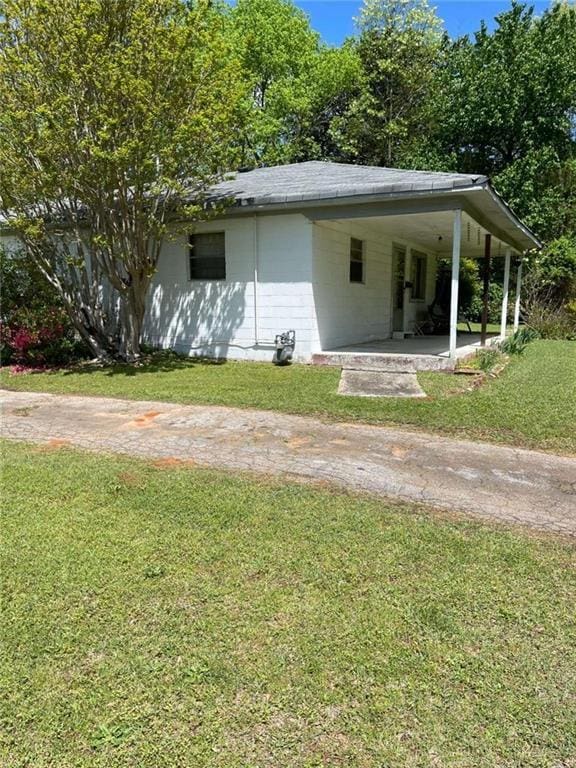 exterior space featuring a carport, concrete block siding, driveway, and a lawn