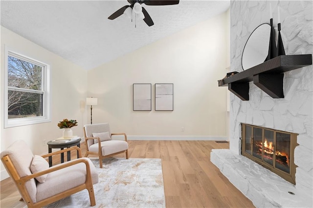 living area with lofted ceiling, a fireplace, ceiling fan, and light hardwood / wood-style flooring