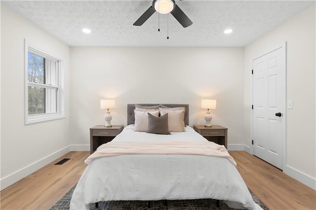 bedroom with a textured ceiling, ceiling fan, and light hardwood / wood-style floors