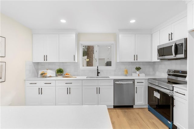 kitchen with stainless steel appliances, white cabinetry, sink, and light hardwood / wood-style flooring