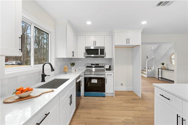 kitchen with light hardwood / wood-style floors, decorative backsplash, white cabinetry, appliances with stainless steel finishes, and sink