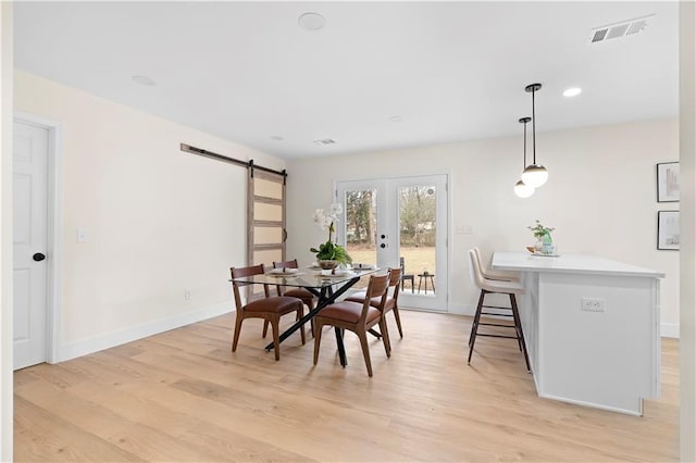 dining space with light wood-type flooring, french doors, and a barn door