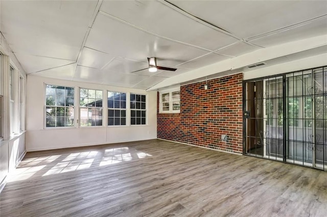 unfurnished sunroom with a wooden deck, visible vents, wood finished floors, and brick wall