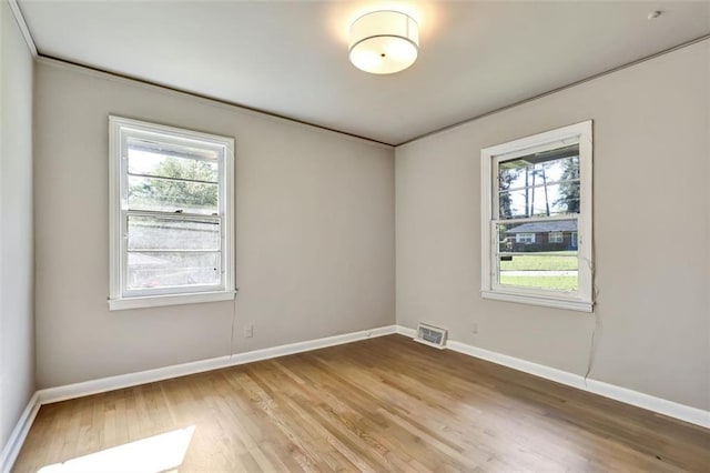 empty room featuring baseboards, visible vents, wood finished floors, and ornamental molding
