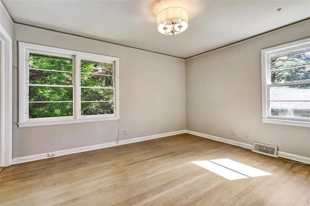 spare room featuring an inviting chandelier, visible vents, light wood-style flooring, and baseboards