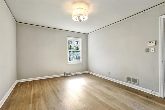 spare room featuring an inviting chandelier, wood finished floors, visible vents, and baseboards