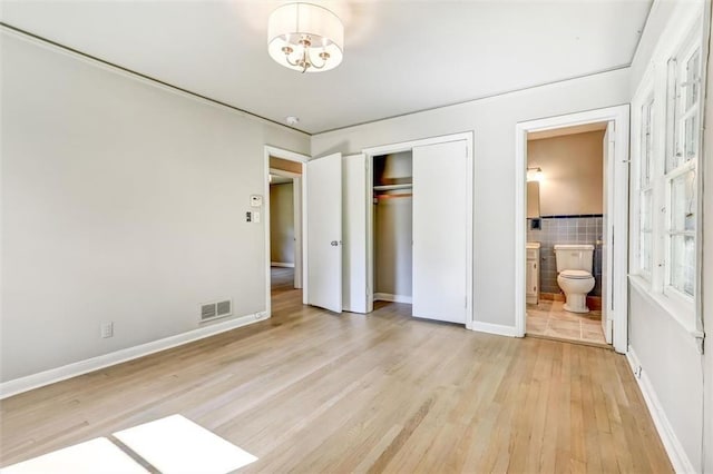 unfurnished bedroom with visible vents, ensuite bathroom, baseboards, a closet, and light wood-type flooring