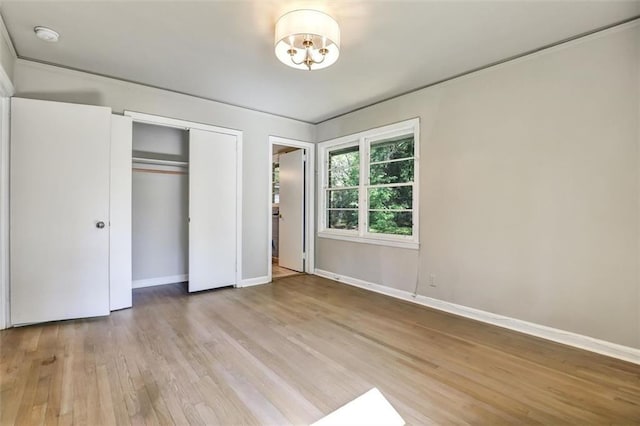 unfurnished bedroom featuring wood finished floors, a closet, a chandelier, and baseboards