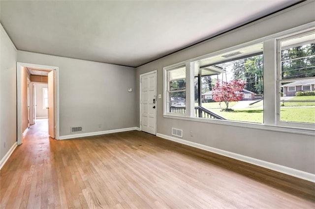 unfurnished room featuring wood finished floors, visible vents, a healthy amount of sunlight, and baseboards