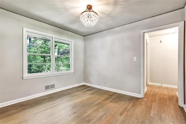 empty room with an inviting chandelier, visible vents, light wood-style floors, and baseboards