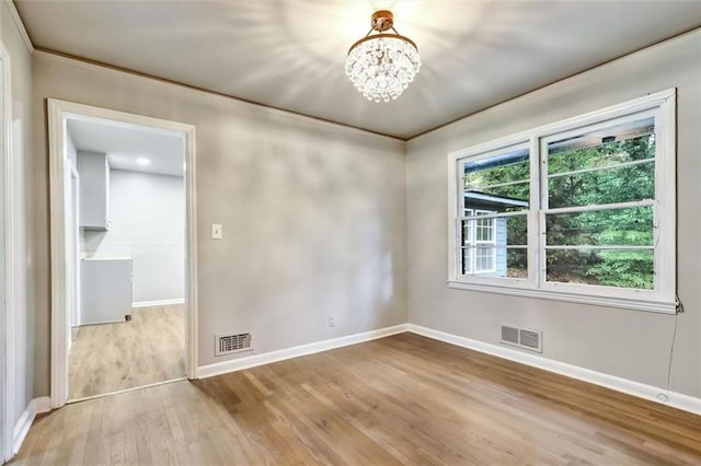 unfurnished room featuring an inviting chandelier, wood finished floors, visible vents, and baseboards