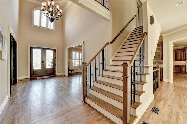 entrance foyer featuring a high ceiling, a notable chandelier, french doors, light wood-type flooring, and ornamental molding