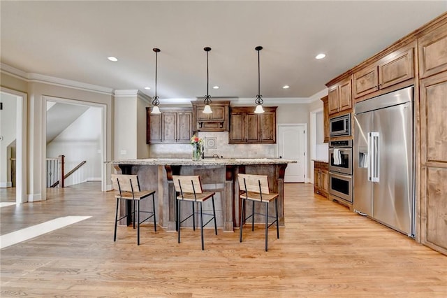 kitchen with built in appliances, decorative light fixtures, a breakfast bar area, decorative backsplash, and a kitchen island with sink