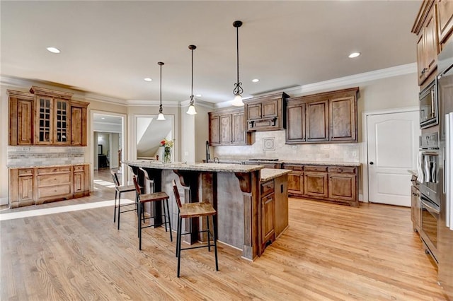 kitchen featuring light stone counters, tasteful backsplash, hanging light fixtures, and an island with sink