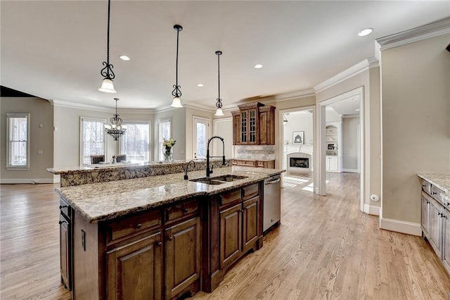 kitchen featuring sink, decorative light fixtures, dishwasher, light stone countertops, and a center island with sink