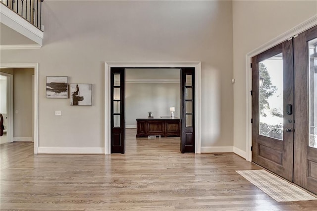 foyer entrance featuring french doors, light wood-type flooring, and crown molding