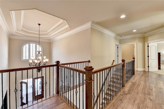 corridor with light hardwood / wood-style floors, ornamental molding, a tray ceiling, and a notable chandelier