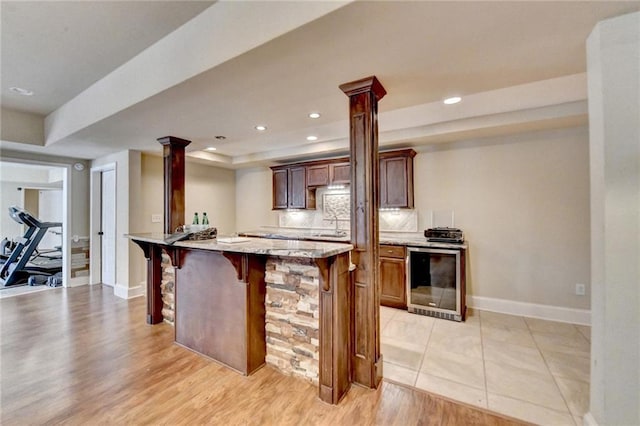 kitchen featuring light stone countertops, a kitchen bar, light wood-type flooring, wine cooler, and sink