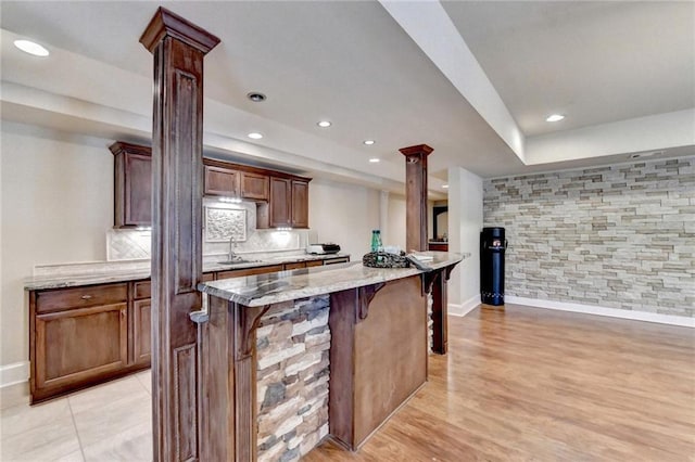 kitchen featuring a kitchen island, decorative columns, light stone countertops, and a breakfast bar