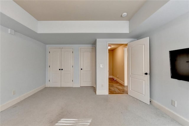 unfurnished bedroom with a raised ceiling, a closet, and light colored carpet