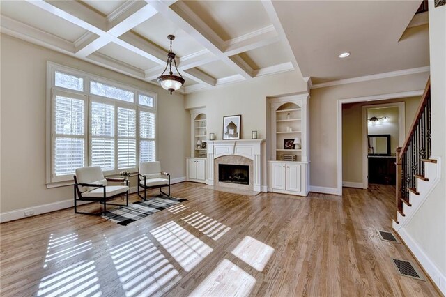 sitting room featuring beamed ceiling, light wood-type flooring, coffered ceiling, a high end fireplace, and crown molding