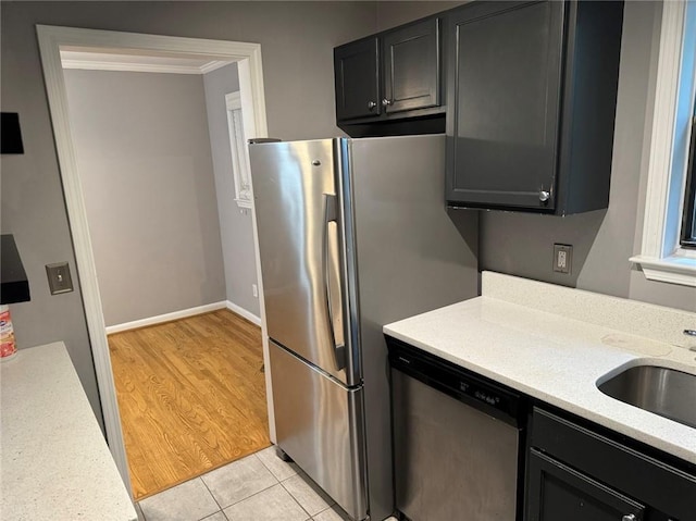 kitchen with light stone countertops, stainless steel appliances, sink, light tile patterned flooring, and crown molding