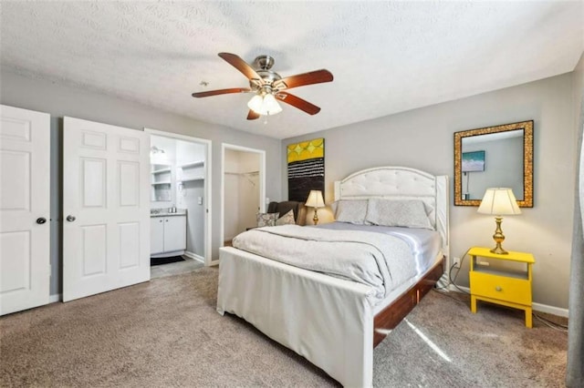 carpeted bedroom featuring ceiling fan, ensuite bathroom, a textured ceiling, a walk in closet, and a closet