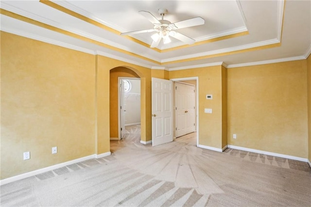 empty room featuring a tray ceiling, crown molding, arched walkways, and carpet floors