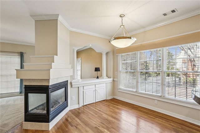 interior space featuring visible vents, baseboards, a multi sided fireplace, ornamental molding, and light wood-style flooring