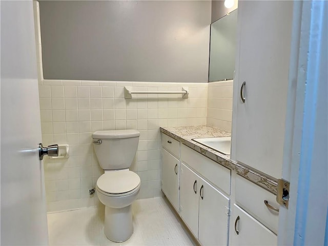 bathroom featuring toilet, tile walls, wainscoting, and vanity