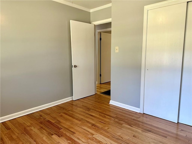 unfurnished bedroom with a closet, baseboards, ornamental molding, and light wood-type flooring