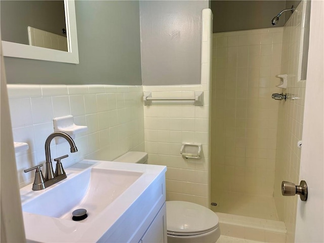 full bathroom featuring tile walls, wainscoting, a tile shower, vanity, and toilet