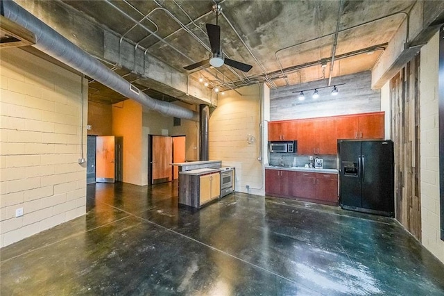 kitchen with finished concrete flooring, appliances with stainless steel finishes, a ceiling fan, and concrete block wall