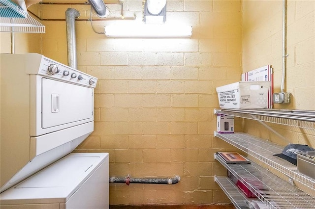 washroom with laundry area, stacked washer / dryer, and concrete block wall