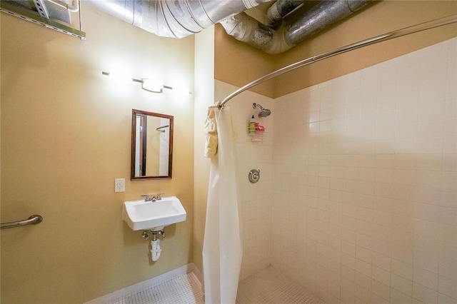 bathroom featuring tile patterned flooring, baseboards, a tile shower, and a sink