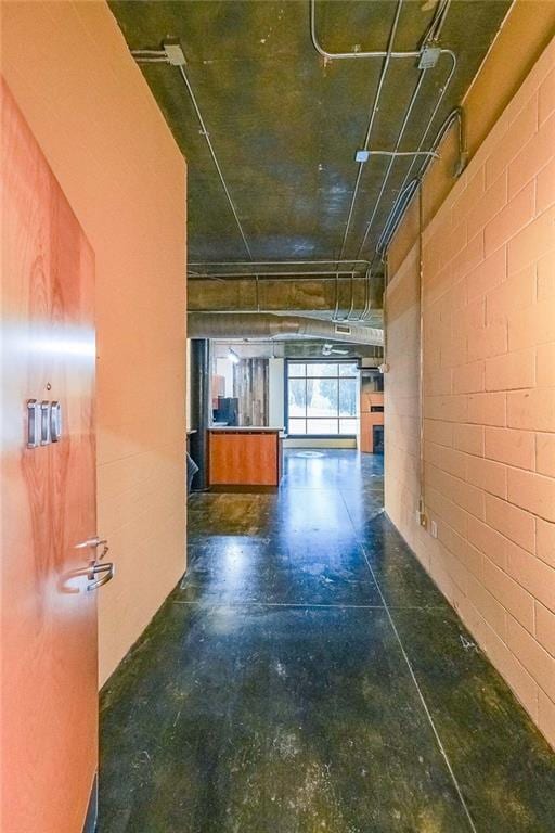 hall featuring concrete block wall and concrete flooring