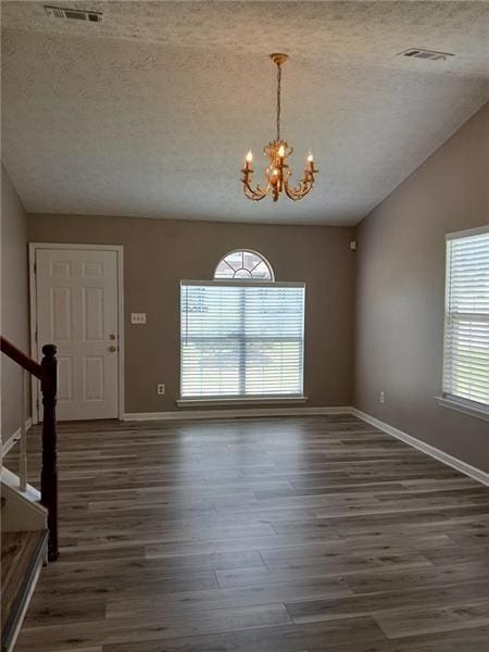 entryway featuring a textured ceiling, a chandelier, wood finished floors, baseboards, and lofted ceiling