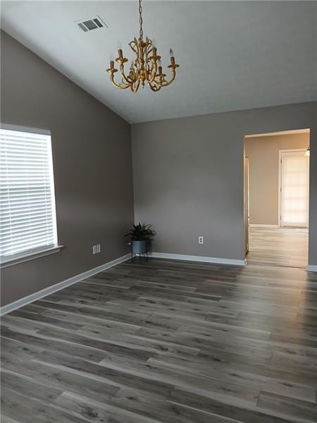 empty room with vaulted ceiling, baseboards, wood finished floors, and a chandelier