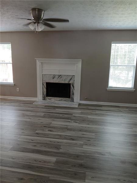unfurnished living room featuring baseboards, a textured ceiling, wood finished floors, a ceiling fan, and a high end fireplace