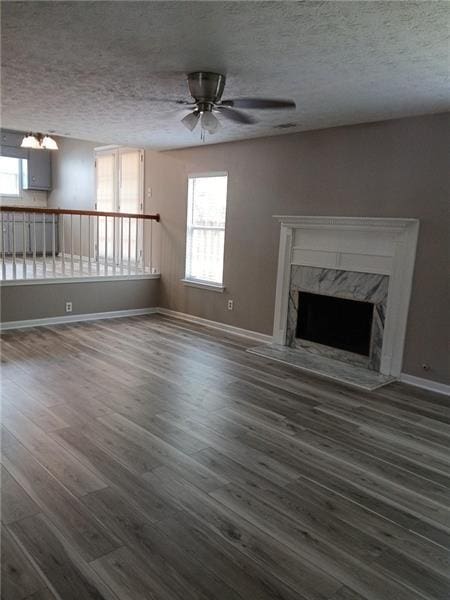 unfurnished living room featuring a ceiling fan, dark wood-type flooring, a fireplace, a textured ceiling, and baseboards