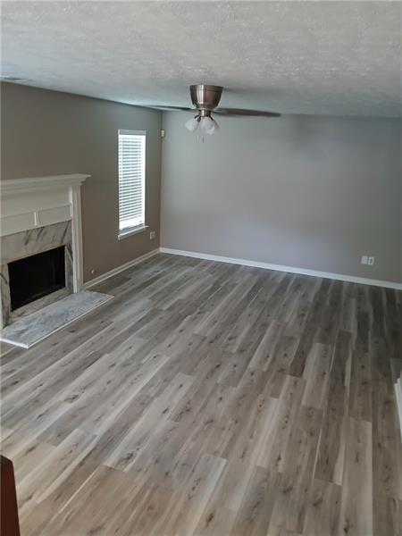 unfurnished living room featuring wood finished floors, a high end fireplace, ceiling fan, a textured ceiling, and baseboards