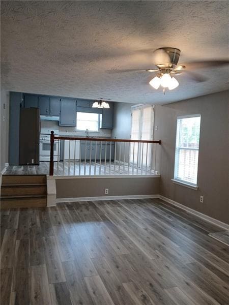 unfurnished living room with a textured ceiling, dark wood-style floors, a sink, a ceiling fan, and baseboards