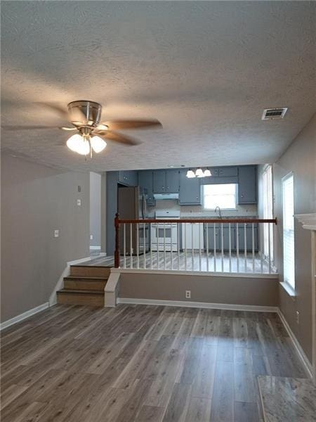 empty room featuring a textured ceiling, dark wood-type flooring, ceiling fan, baseboards, and stairway
