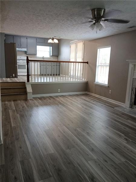 unfurnished living room featuring plenty of natural light, a ceiling fan, dark wood-style floors, a textured ceiling, and a fireplace