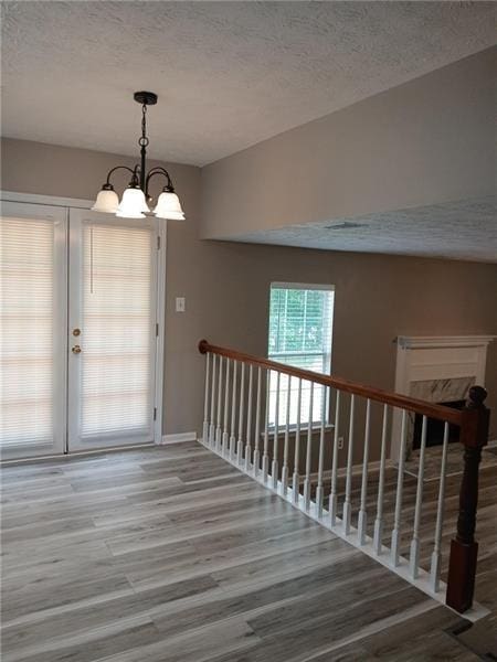 interior space with wood finished floors, a textured ceiling, a chandelier, and baseboards