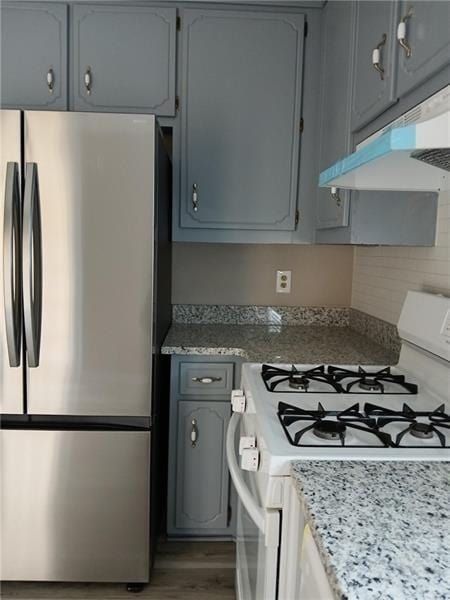 kitchen featuring freestanding refrigerator, white gas range, under cabinet range hood, and gray cabinets